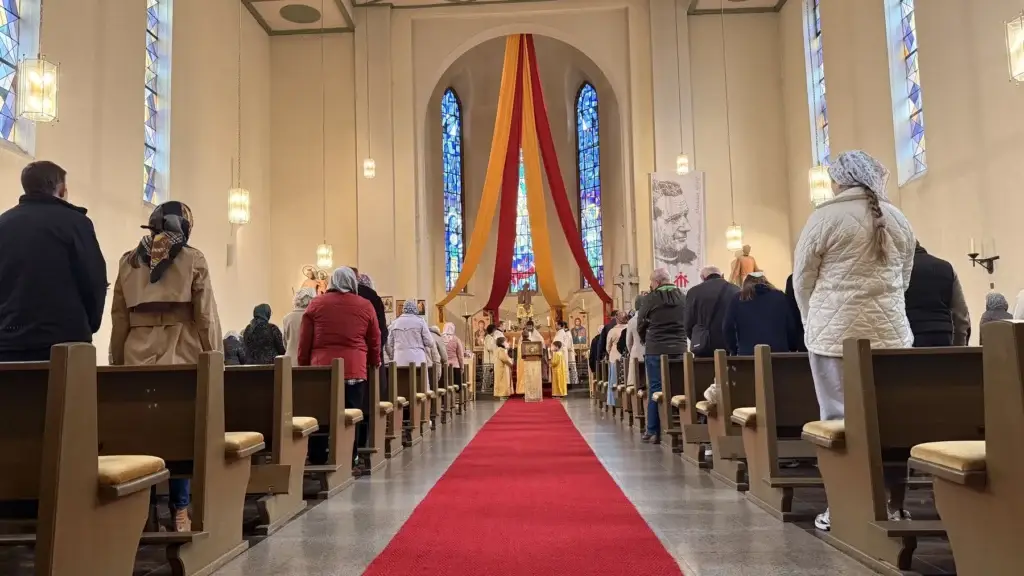 Gottesdienst in der Don-Bosco-Kirche in Würzburg: Die Gemeinde steht in den Bänken, viele Frauen tragen ein Kopftuch, vorn Priester und Altardiener in goldenen Gewändern