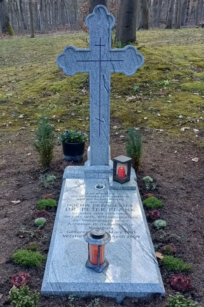 Grab von Vater Peter auf dem Würzburger Waldfriedhof: hohes Kreuz aus hellem Granit mit eingraviertem orthodoxem Kreuz, davor die Grabplatte mit seinem Namen, zwei Grablaternen mit rotem Licht und frisch bepflanzte Erde